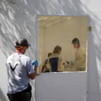 Medical staff from Global Response Management take samples from a patient suspected of contracting COVID-19 at a migrant encampment, where more than 2,000 people live while seeking asylum in the U.S., in Matamoros, Mexico, on May 1. | REUTERS 