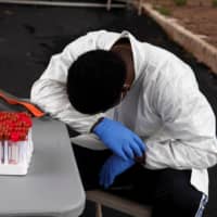 A health care worker takes a break as people wait in their vehicles in long lines to get tested for COVID-19 in Houston on Tuesday.  | REUTERS