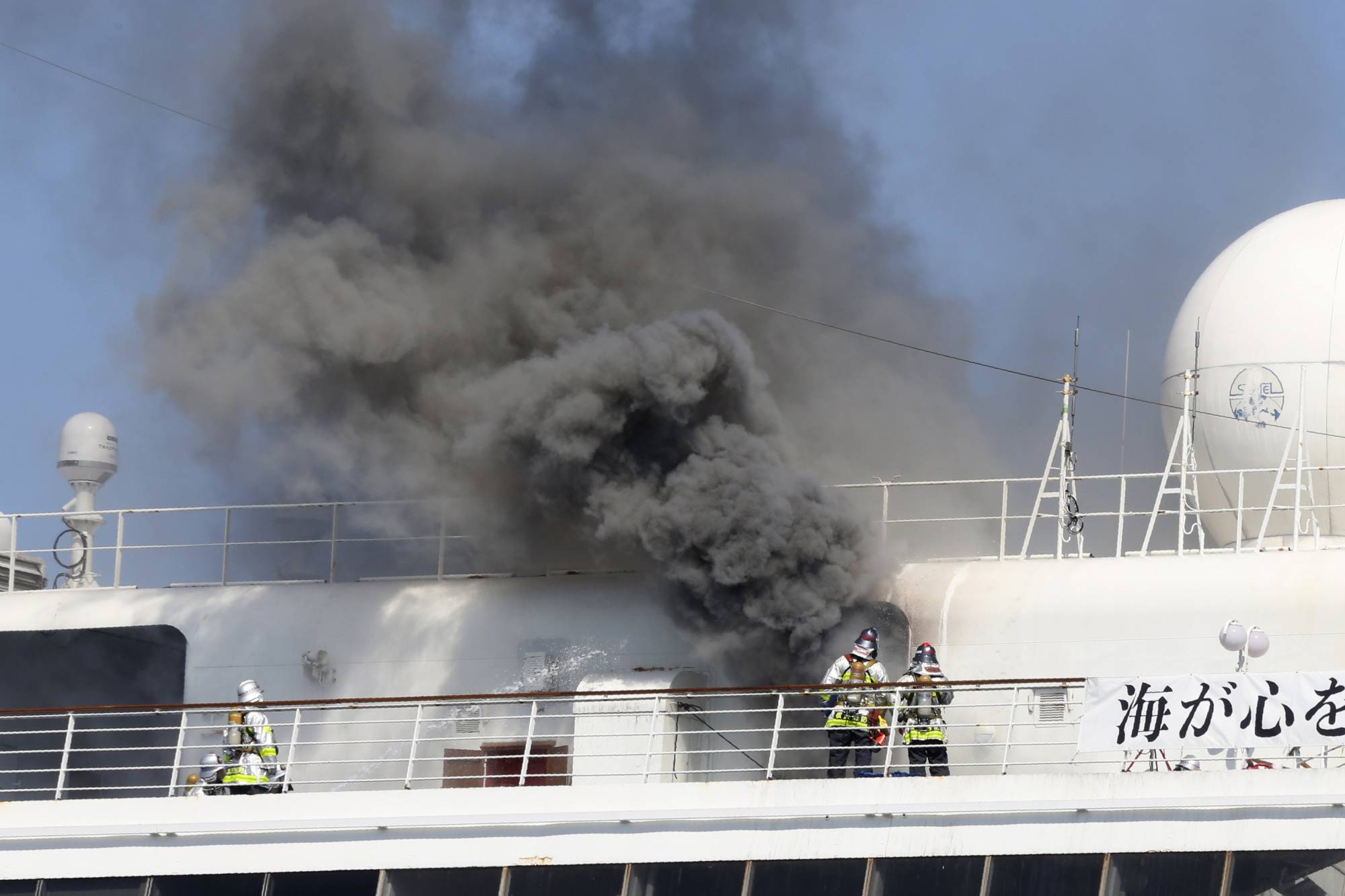 Smoke rises from the Japanese cruise ship Asuka II, docked in Yokohama Port, on June 16. Finding places to park idle ships is just the first painful point. To keep things shipshape and avoid costly repairs and other issues, the vessels must also be kept operating. | AP