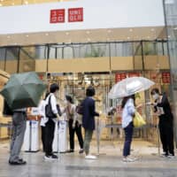 Customers queue to collect tickets allowing them to purchase Uniqlo AIRism masks at a Uniqlo store, operated by Fast Retailing Co., in Tokyo last month. | BLOOMBERG
