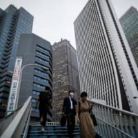 The skyscrapers of Shinjuku tower over passersby on the stairs in Tokyo on June 24 as the coronavirus pandemic causes companies to question the future of the office. | REUTERS
