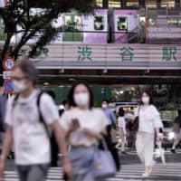 People wearing face masks walk outside JR Shibuya Station on Friday. Tokyo confirmed 206 new cases of COVID-19 on Saturday. | BLOOMBERG