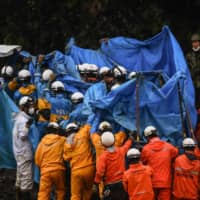 Rescue workers hold up a blue sheet as they recover a victim\'s body during a search for people still missing in Fukuhama, Kumamoto Prefecture, on Saturday after torrential rains spurred floods and landslides devastated the region earlier in the week. | AFP-JIJI