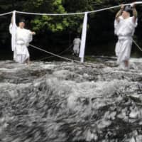Shinto priests dressed in traditional costume take part in an event to exchange a shimenawa sacred rope that spans the river above Nachi Falls in Nachikatsuura, Wakayama Prefecture, on Monday. | KYODO