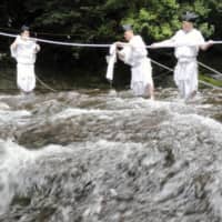 Shinto priests dressed in traditional costume take part in an event to exchange a shimenawa sacred rope that spans the river above Nachi Falls in Nachikatsuura, Wakayama Prefecture, on Monday. | KYODO