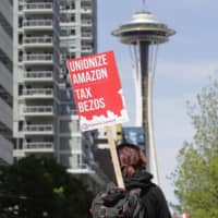 A protester carries a sign that reads \"Unionize Amazon Tax Bezos\" during a protest in downtown Seattle on May 1.  | AP