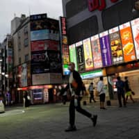A man wearing a face mask makes his way through the Kabukicho district of Tokyo\'s Shinjuku Ward on Tuesday. The capital confirmed 165 new COVID-19 cases on Wednesday. | REUTERS
