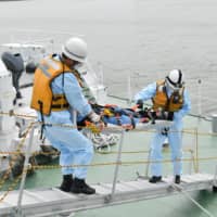 Japan Coast Guard officers carry a stretcher aboard a ship during a drill held Monday in Izumiotsu, Osaka Prefecture, under the scenario that a passenger of a ferry was suspected of being infected with COVID-19. | KYODO