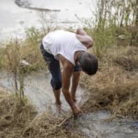 A farmhand inspects the ground as water is being pumped from a bore well to flood a rice field at a farm in Karnal district, Haryana, India, on June 26. A scarcity of workers this year because of the coronavirus is forcing Indian farmers to turn away from traditional methods of farming. | BLOOMBERG