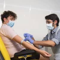 A doctor takes blood samples for use in a coronavirus vaccine trial in Oxford, England, on June 25. | UNIVERSITY OF OXFORD / VIA AP