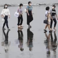 People wearing face masks walk on a beach in Fujisawa, Kanagawa Prefecture. Including Kanagawa, prefectures in the Tokyo metropolitan area have recently seen rises in the number of COVID-19 cases. | AP