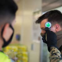 A U.S. Marine conducts a temperature check at the front of the commissary at Camp Courtney in Okinawa Prefecture on July 13. | U.S. MARINE CORPS