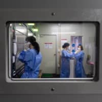 A medical worker speaks with a visitor from inside the Covid-19 safety booth at a walk-thru testing center at H Plus Yangji Hospital in Seoul on Friday. | BLOOMBERG
