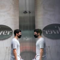 A man passes in front of Pfizer Inc.\'s headquarters in New York on July 22. U.S. health officials agreed pay $1.95 billion for 100 million doses of a vaccine made by Pfizer Inc. and BioNTech SE. There are more than 160 coronavirus vaccines in development, according to the World Health Organization, though only 25 are currently in human studies. | BLOOMBERG