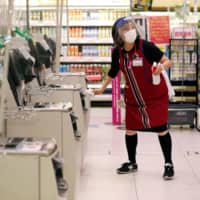 An employee wearing a protective mask and face shield uses an alcohol-based solution to clean automated checkout counters in an Aeon shopping mall in Chiba on May 28. | REUTERS