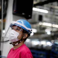 An employee with a protective mask and face shield works on the assembly line at the Mitsubishi Fuso Truck and Bus Corp. factory in Kawasaki on May 18. | REUTERS