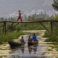 A Kashmiri woman walks back home after buying bread as men row their boat after selling their vegetables at the floating vegetable market on the Dal Lake in Srinagar, India.  | AP
