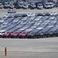 A worker stands as Honda Motor vehicles bound for shipment sit parked at a port in Yokohama on July 19. | BLOOMBERG