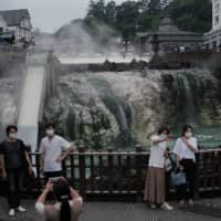 People pose in front of the source of a hot spring at Kusatsu Onsen in Kusatsu, Gunma Prefecture, on June 27. | BLOOMBERG