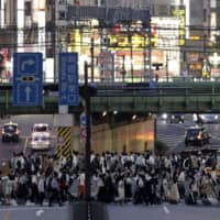 Pedestrians cross a road as dusk falls in Tokyo\'s Shinjuku district on July 10. | BLOOMBERG