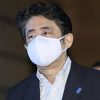 Prime Minister Shinzo Abe arrives at his office in Tokyo on Saturday wearing a cloth mask larger than his trademark \"Abenomask\" distributed to ward off the novel coronavirus. | KYODO