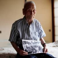 Lee Hak-rae, the last surviving Korean war criminal from World War II, holds a copy of a photo that was taken at a POW camp run by the Japanese Imperial Army in Thailand in 1942, during an interview at his home in Tokyo.  | REUTERS
