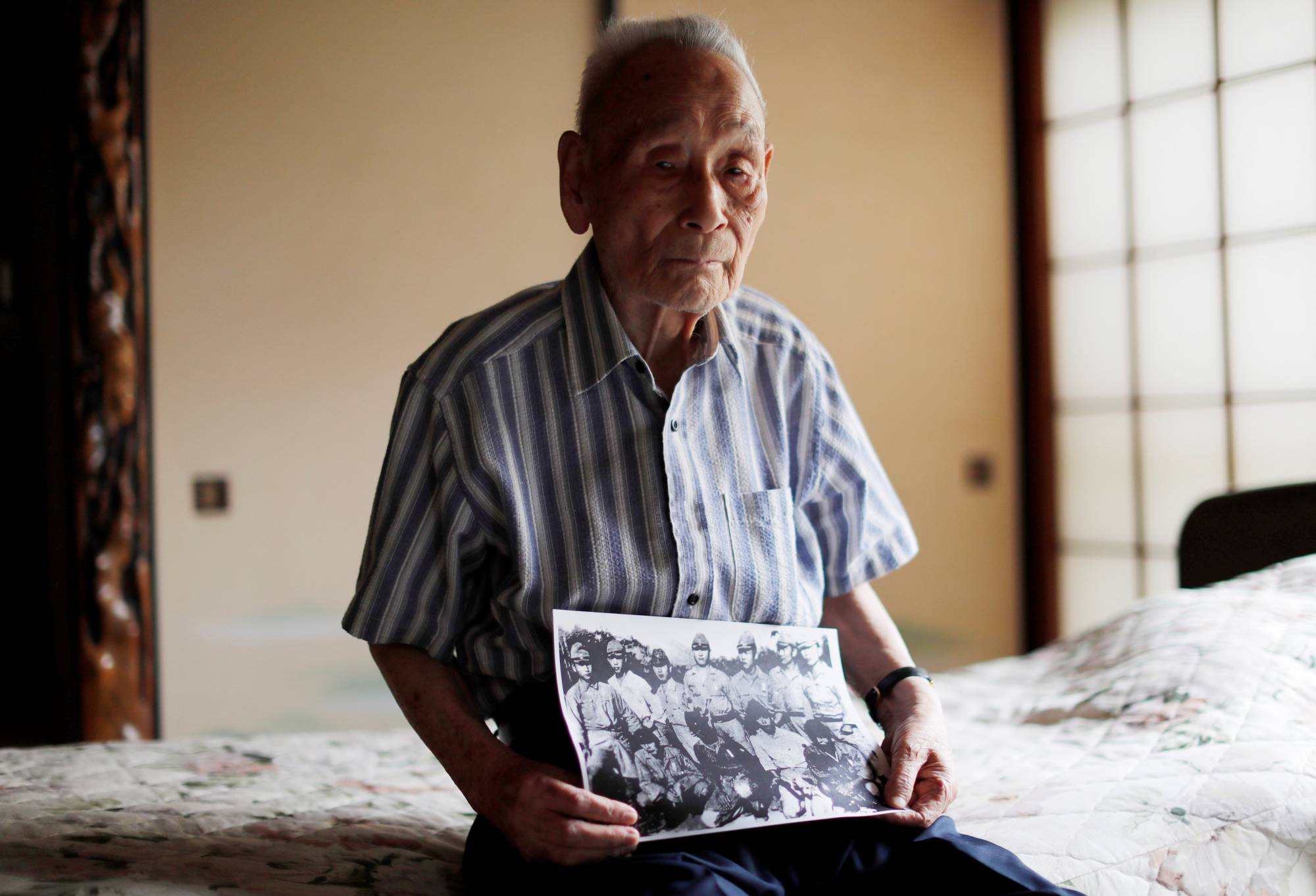 Lee Hak-rae, the last surviving Korean war criminal from World War II, holds a copy of a photo that was taken at a POW camp run by the Japanese Imperial Army in Thailand in 1942, during an interview at his home in Tokyo.  | REUTERS