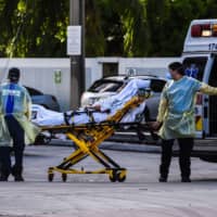 Medics transfer a patient on a stretcher from an ambulance outside of a hospital near Miami.  | AFP-JIJI