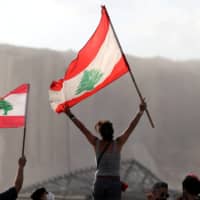 Demonstrators wave Lebanese flags during protests on Tuesday near the site of the blast in Beirut\'s port area.  | REUTERS 