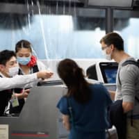 Staff assist passengers from behind a plastic barrier at the Air France-KLM Group check-in desk at Narita Airport in Narita, Chiba Prefecture, on July 19. | BLOOMBERG