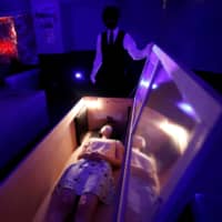 A participant lies inside a mock coffin with plastic shields to maintain social distancing during a coffin horror show performed by Kowagarasetai (Scare Squad) in Tokyo on Saturday. | REUTERS