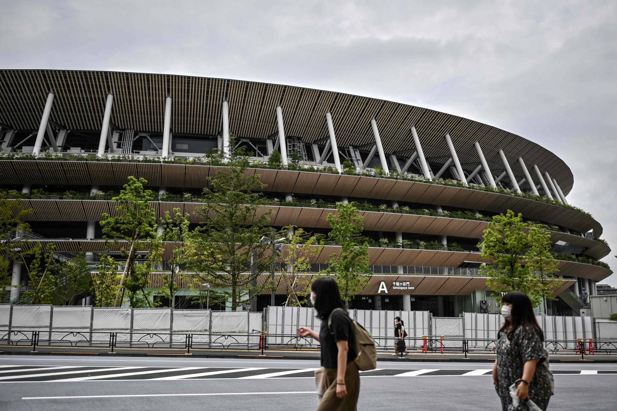 People walk past the National Stadium, the main venue for the 2020 Olympic and Paralympic Games now postponed due to the coronavirus pandemic, in Tokyo on Sunday. | AFP-JIJI