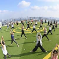 About 50 people take part in a morning yoga session on the rooftop of the Shibuya Sky building in Tokyo on Aug. 26, before going to work. | KYODO