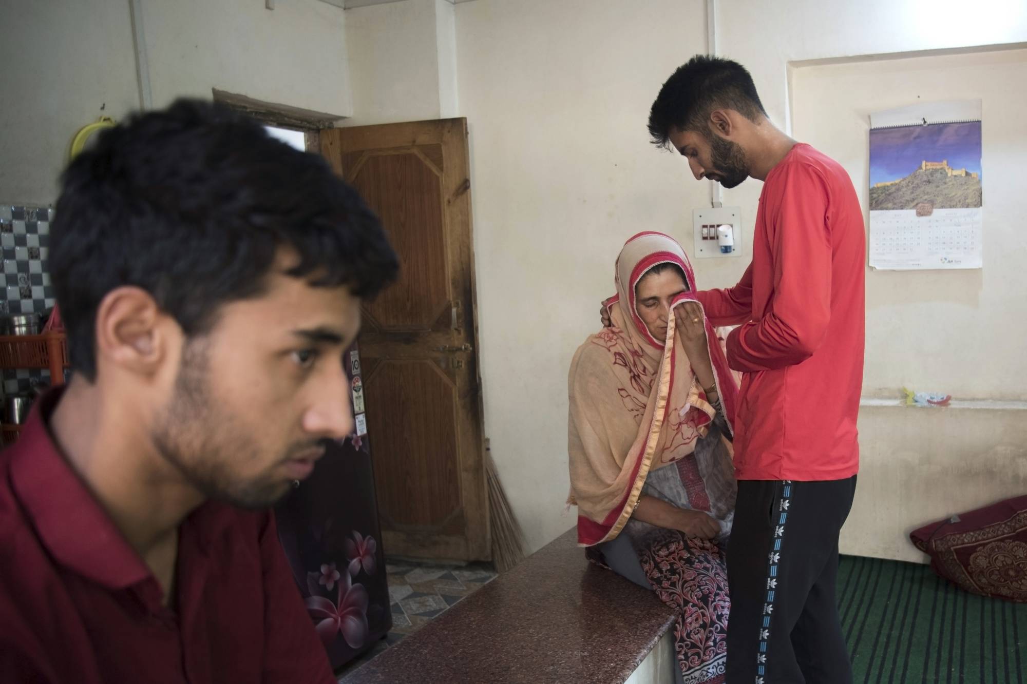 Shaheen Sajad is comforted by her eldest son, Sameer Ahmad, while her youngest son Salman Sajad looks on at their house in Vessu, India. | Showkat Nanda/The New York Times