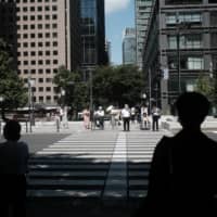 People wait to cross an intersection in Tokyo\'s Marunouchi business district in August. | BLOOMBERG