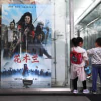 Children play next to a poster of the Disney movie \"Mulan\" outside a cinema in Beijing on Friday. | AFP-JIJI