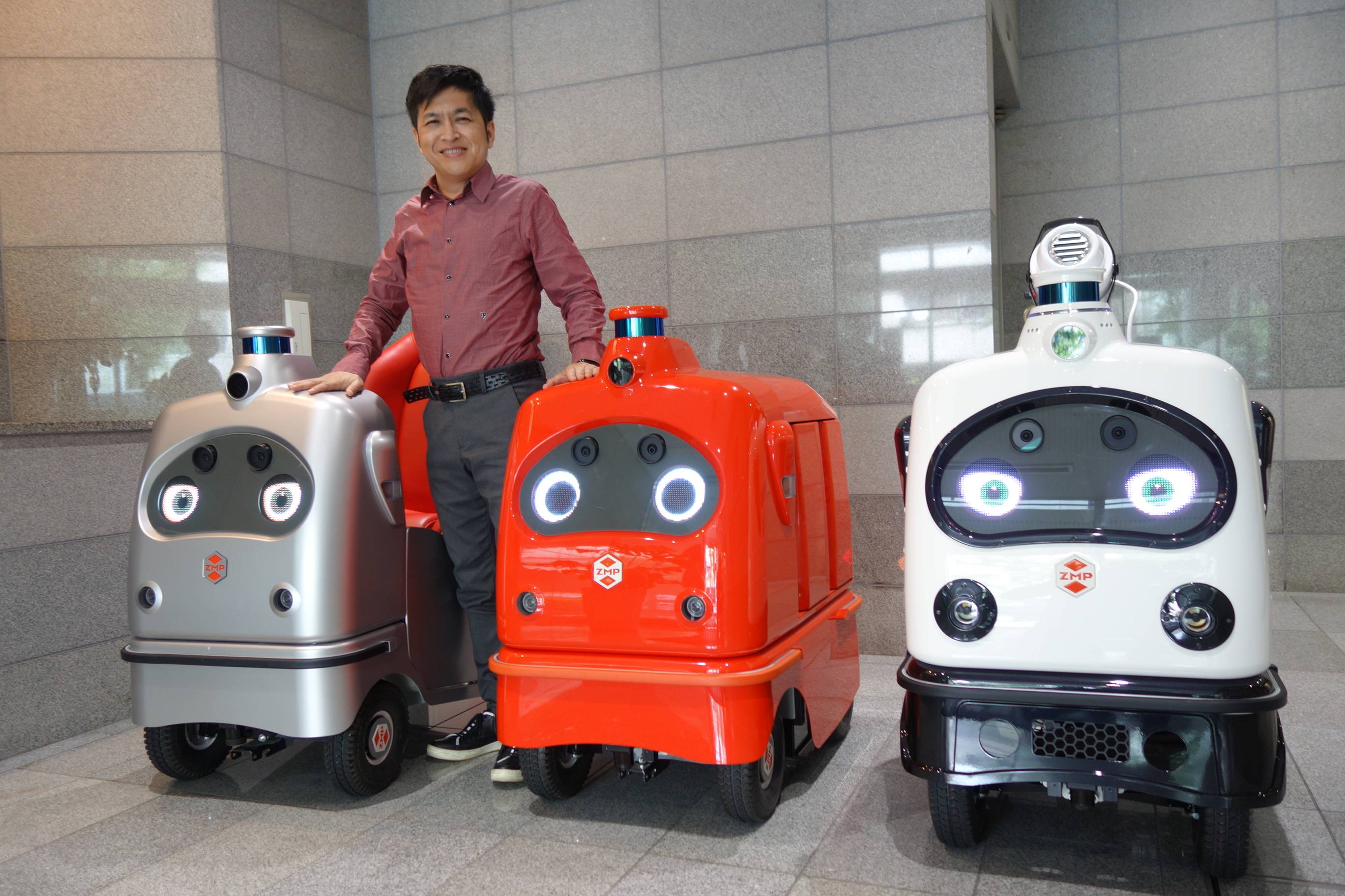 Hisashi Taniguchi, CEO of ZMP Inc., stands with the service robots his company has produced at its headquarters in Bunkyo Ward. | ALEX MARTIN