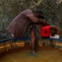 Carlos Augusto Rodrigues, 35, gives Rafael Silva, 16, a bottle filled with water to help put out a fire on a ranch in the Pantanal. | REUTERS 