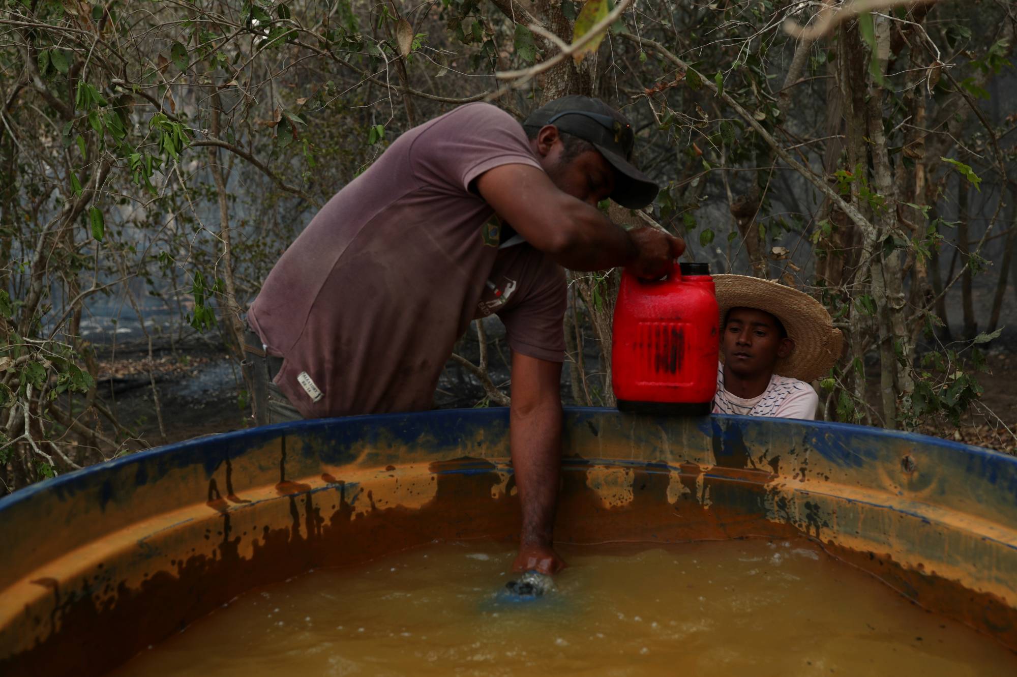 Carlos Augusto Rodrigues, 35, gives Rafael Silva, 16, a bottle filled with water to help put out a fire on a ranch in the Pantanal. | REUTERS 