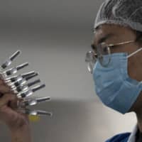 An employee manually inspects syringes of the COVID-19 vaccine produced by SinoVac at its factory in Beijing on Thursday. | AP
