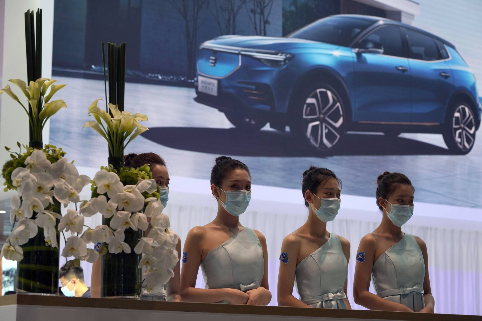 Receptionists with Chinese automaker Enovate wait for attendees of the Auto China 2020 show in Beijing on Saturday. | AP