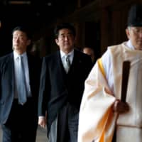 Then-Prime Minister Shinzo Abe is led by a Shinto priest as he visits Yasukuni Shrine in Tokyo in December 2013. | REUTERS