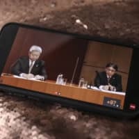 Jun Sawada (left), president and chief executive officer of Nippon Telegraph and Telephone Corp., and Kazuhiro Yoshizawa, president and chief executive officer of NTT Docomo Inc., attend a news conference, as seen on a smartphone in Tokyo on Tuesday. | BLOOMBERG
