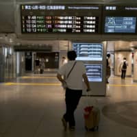 A passenger looks at a departure information board for East Japan Railway Co. bullet trains at Tokyo Station. | BLOOMBERG