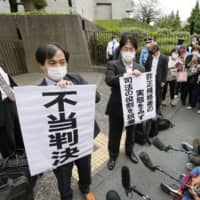 Supporters of the plaintiff hold a sign reading \"unjust ruling\" on Tuesday in Tokyo after the Supreme Court ruled against a non-regular worker who sued her employer for not paying her bonuses. | KYODO
