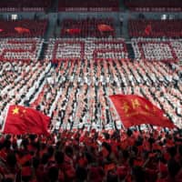 First-year students wave Chinese flags during a commencement ceremony in China\'s Hubei province last month. | AFP-JIJI