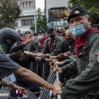 Pro-democracy protesters struggle to remove barriers during a street march in Bangkok on Wednesday. | AP