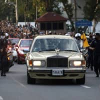 A vehicle carrying Thailand\'s King Maha Vajiralongkorn and Queen Suthida drives past an anti-government mass protest in Bangkok on Wednesday.  | REUTERS 