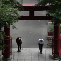 People wearing protective masks to help curb the spread of the COVID-19 virus bow before climbing the steep stairs of a shrine on Oct. 12 in Tokyo. | AP