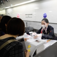 A Japan Airlines Co. employee assists passengers at Narita Airport in Chiba Prefecture on Sept. 26. | BLOOMBERG